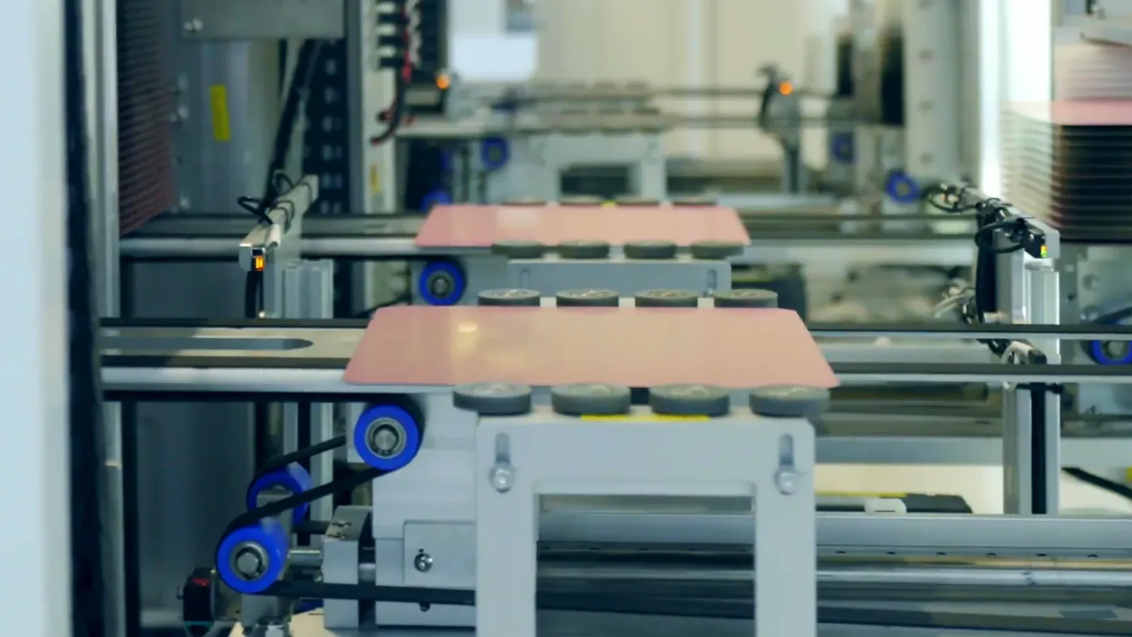 Looking down an automated cell: two pink boards on a carriage between white machine frames, blue rollers in the foreground, nobody in the frame, stock footage with an illustration of event lines and boxes