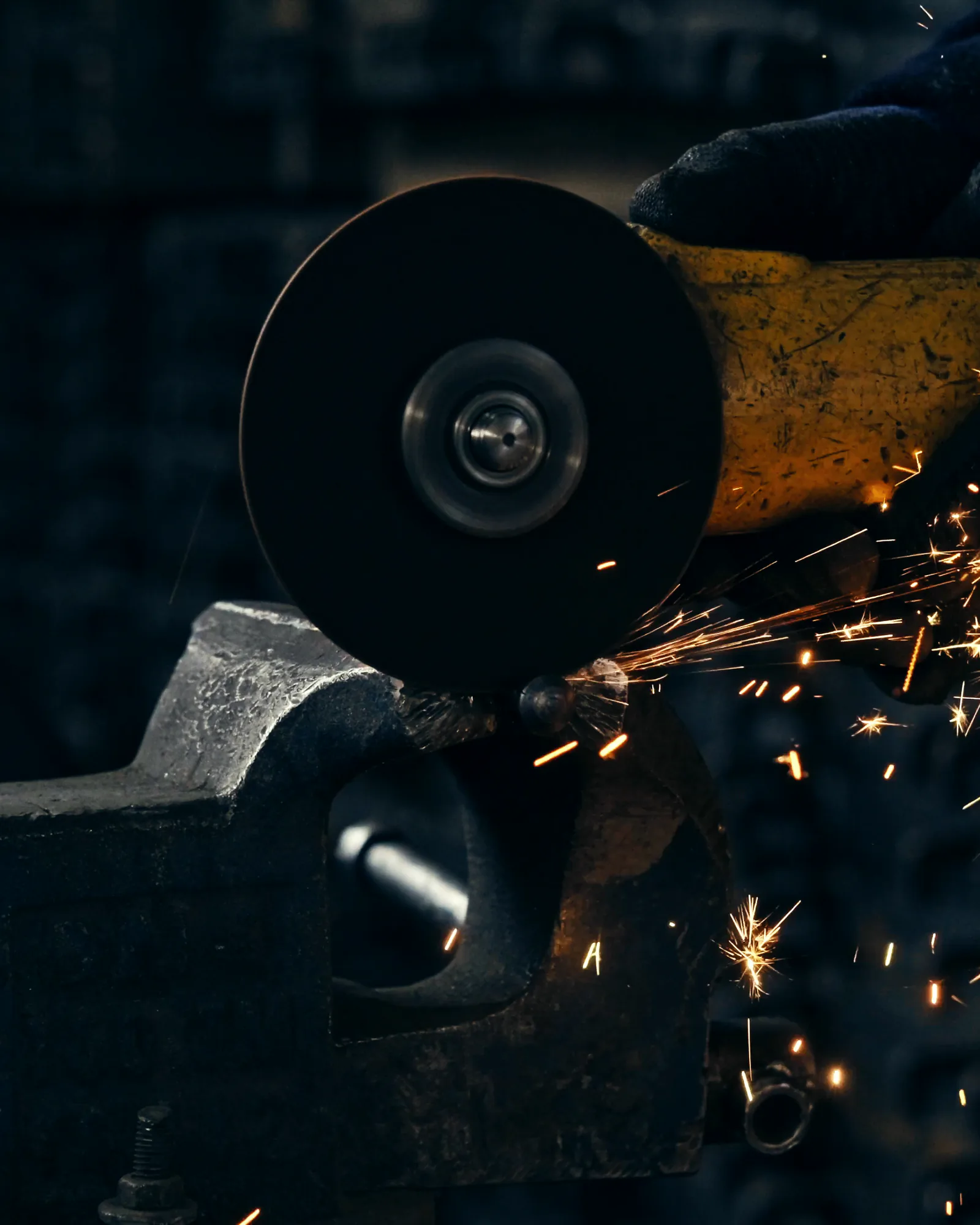 A close view of an angle grinder cutting a bar held in a vice, a gloved hand at the top right and a spray of sparks, stock footage
